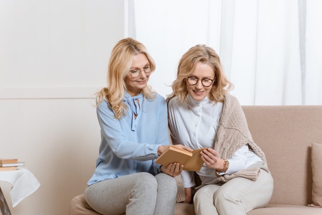 Two middle aged women sitting on sofa and reading book